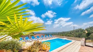Privézwembad met blauwe ligbedden en een tak van een palmprom op de voorgrond bij Villa Santa Maria onder een blauwe lucht met her en der wat wolken.