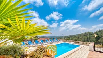 Privézwembad met blauwe ligbedden en een palmblad op de voorgrond bij Villa Santa Maria onder een blauwe lucht met her en der wat wolken.