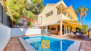 Privézwembad bij Villa Santa Cristina met een betegeld terras, gele zonneschermen en ligbedden op een houten vlonder naast de gele gevel.
