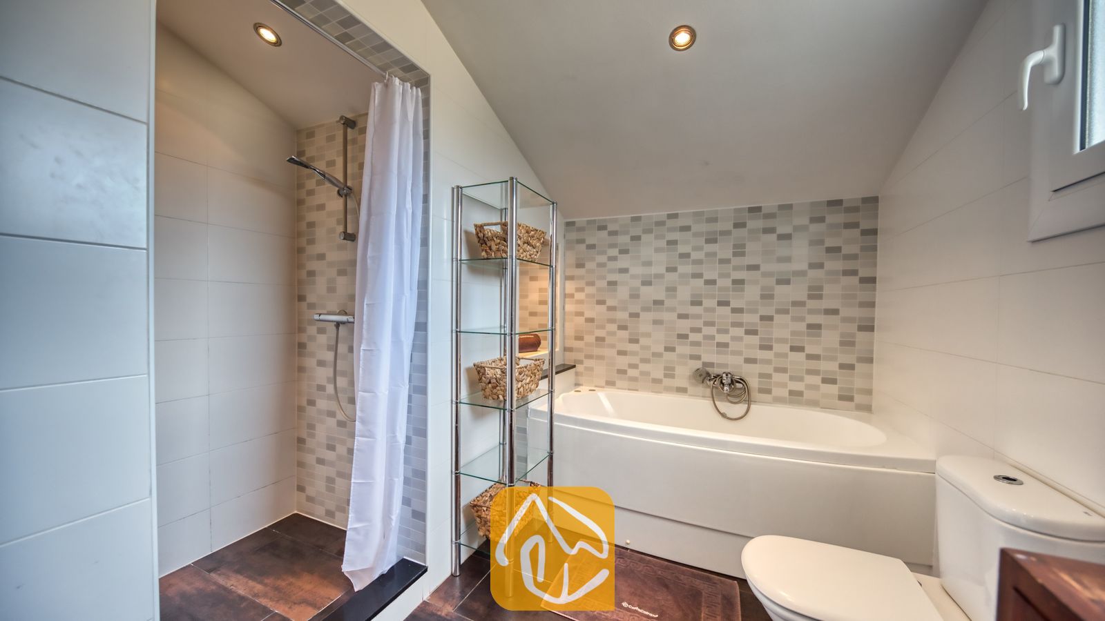 Moderne badkamer met een betegelde inloopdouche met een wit douchegordijn, een wit ligbad, een glazen wandrek met geweven manden en een toilet.
