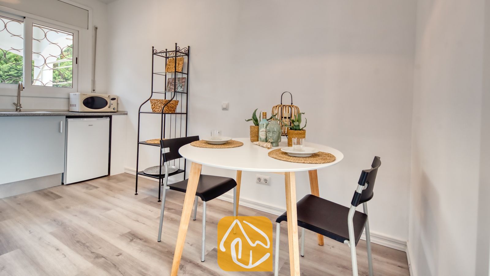 Ronde witte eettafel met houten poten en twee zwarte stoelen, gedekt met geweven placemats en glaswerk in de keuken van Villa Madonna.