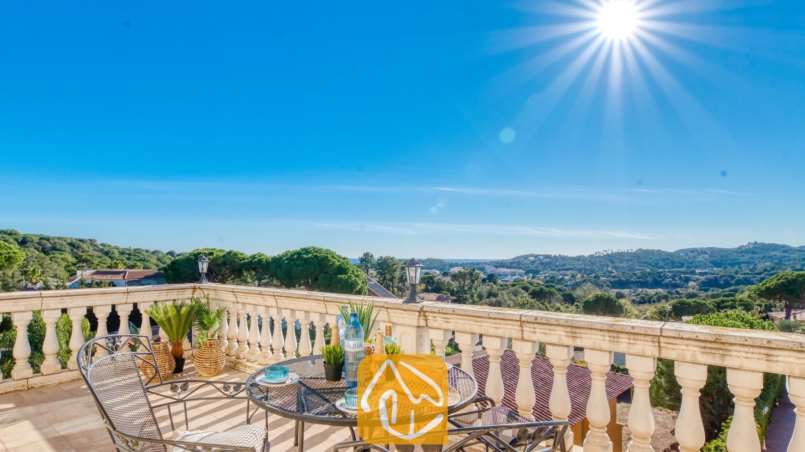 Zonnig terras bij Villa Madonna met een smeedijzeren tafel, strooien hoed en een prachtig uitzicht over de groene vallei onder een helderblauwe hemel.