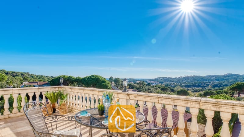 Zonnig terras bij Villa Madonna met een smeedijzeren tafel, strooien hoed en een prachtig uitzicht over de groene vallei onder een helderblauwe hemel.
