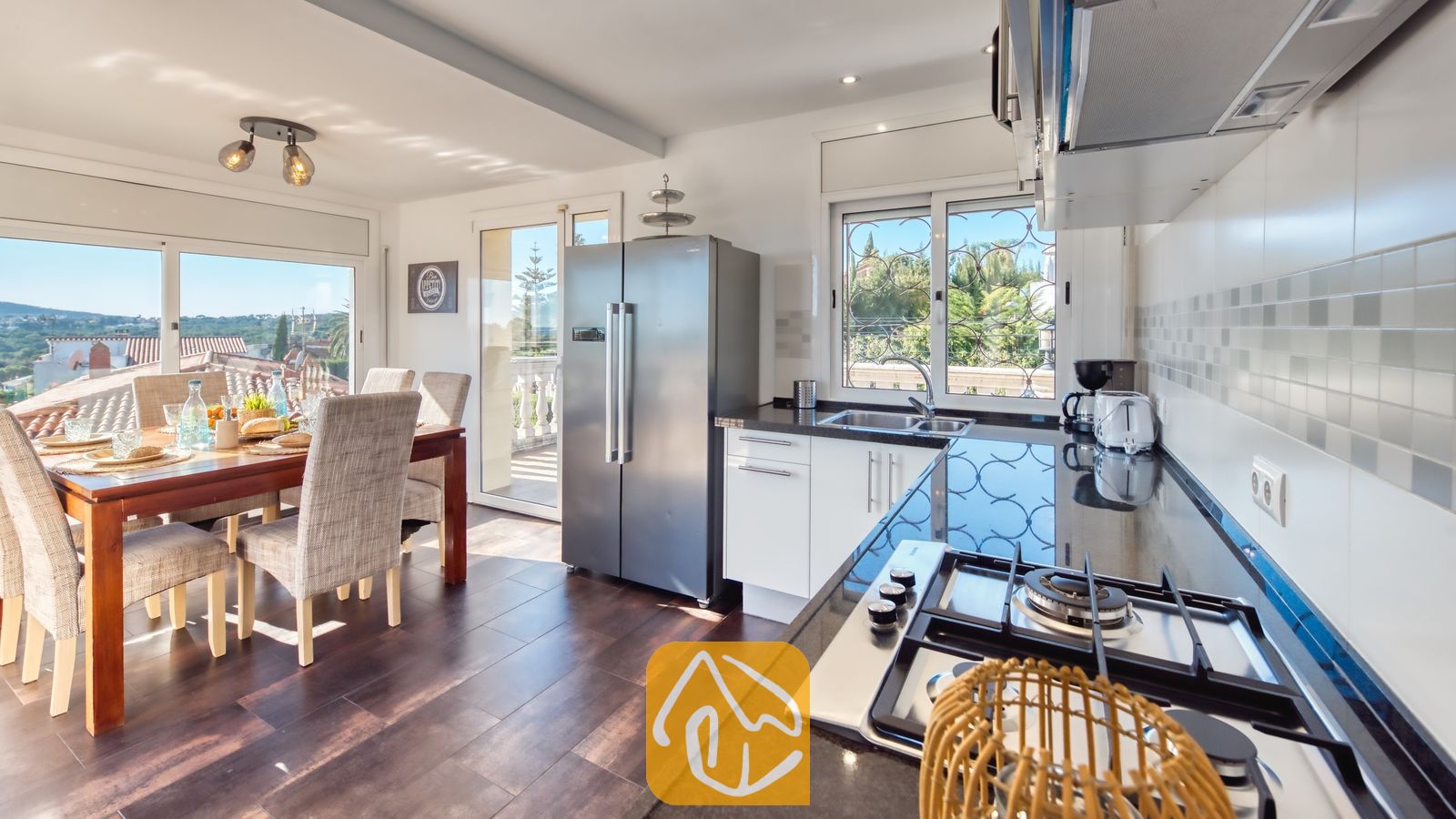 Moderne keuken en eethoek in Villa Madonna met donkere aanrechtbladen, roestvrijstalen apparatuur en een houten eettafel met gestoffeerde stoelen.