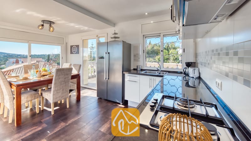 Moderne keuken en eethoek in Villa Madonna met donkere aanrechtbladen, roestvrijstalen apparatuur en een houten eettafel met gestoffeerde stoelen.
