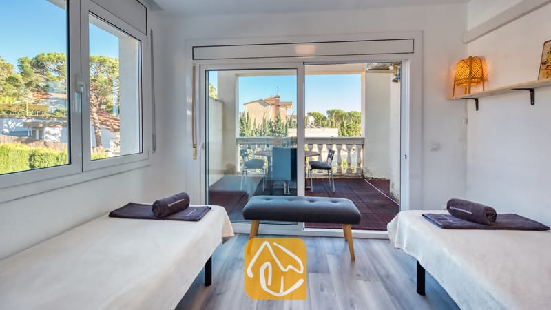 Tweepersoonskamer met twee aparte bedden in Villa Madonna, voorzien van donkergrijze opgerolde handdoeken, een houten bankje en schuifpui naar een balkon.