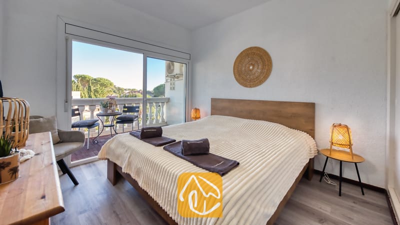 Slaapkamer in Villa Madonna met een houten bed voorzien van een crèmekleurige, geribbelde sprei, geweven bedlampjes en een schuifpui die uitkomt op een balkon.