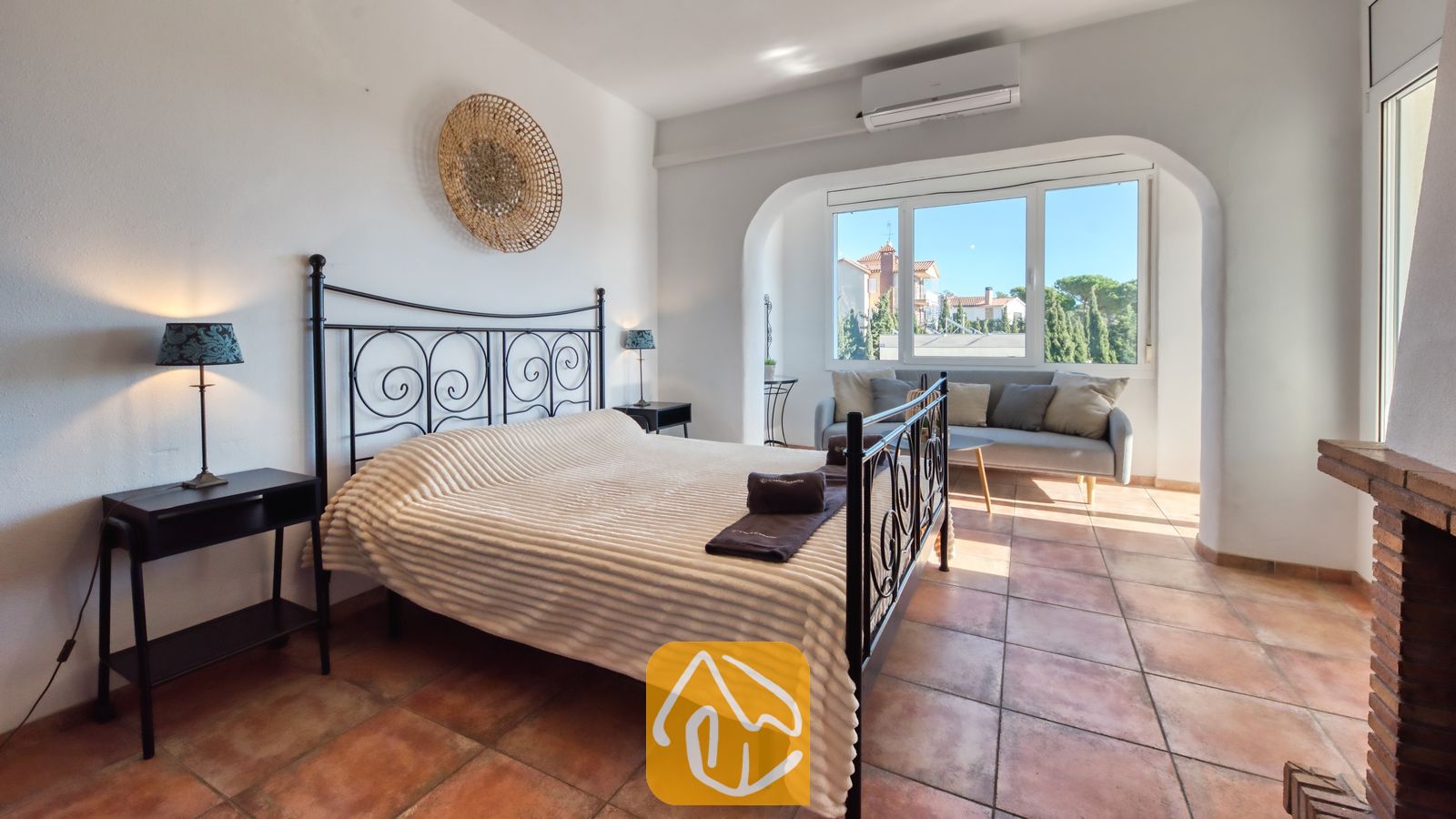 Slaapkamer met een zwart metalen bedframe, een wit geweven deken en terracotta plavuizen.
