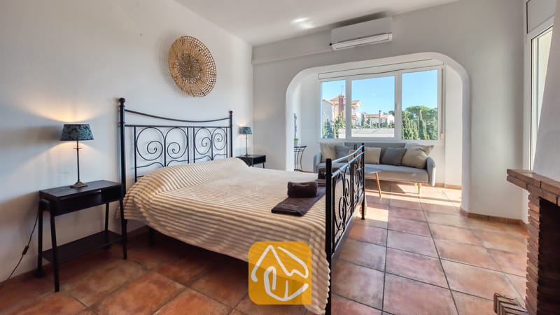 Slaapkamer met een zwart metalen bedframe, een wit geweven deken en terracotta plavuizen.