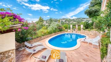 Privézwembad met ligstoelen en betegeld terras bij Villa Cleo in Spanje, omringd door stenen muren en bloeiende struiken.
