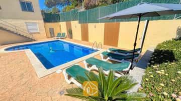 Privé buitenzwembad bij Villa Holiday, omringd door groene ligbedden, een donkere parasol en een stenen terras.