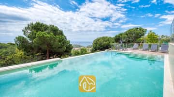 Privézwembad bij Villa BellaVista, voorzien van turkooiskleurige tegels, een zonneterras met glazen omheining en grijze ligbedden, met uitzicht op de zee en de dennenbomen.