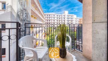 Balkon van Appartement Gaudi met twee witte kunststoftoelen, een klein tafeltje met een plant in pot en een metalen balustrade die uitkijkt over de naburige witte gebouwen.