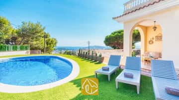 Privézwembad en blauwe houten ligstoelen op kunstgras bij Villa Ibiza met uitzicht op de verre zee en bomen.